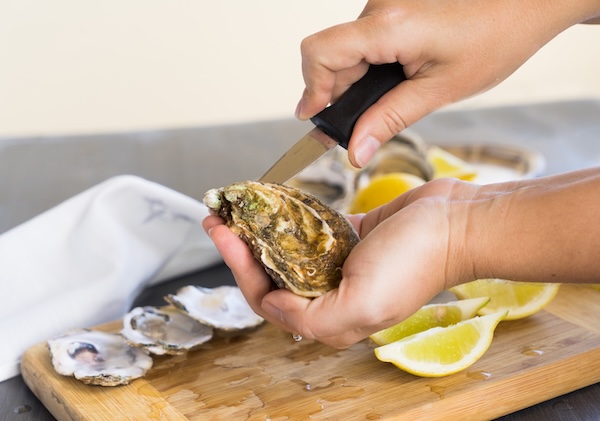 a person using a knife to shuck an oyster all shucked up