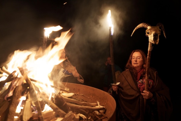 wood sticks burning in a fire as a woman watches Halloween in Ireland