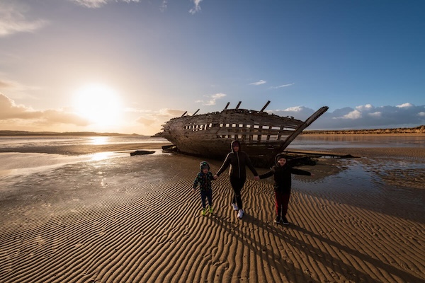 three people standing on a beach with a shipwreck behind them experience Ireland's northwest
